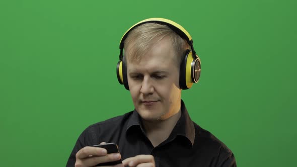 Guy Listens To Music in Wireless Yellow Headphones and Dances. Green Screen