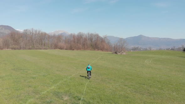 Aerial: man having fun by riding mountain bike in the grass on sunny day, scenic alpine landscape