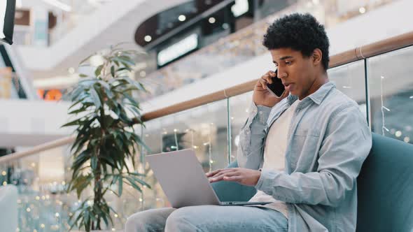 Focused African 30s Freelancer Businessman Talking Smartphone Look at Laptop Screen Pointing