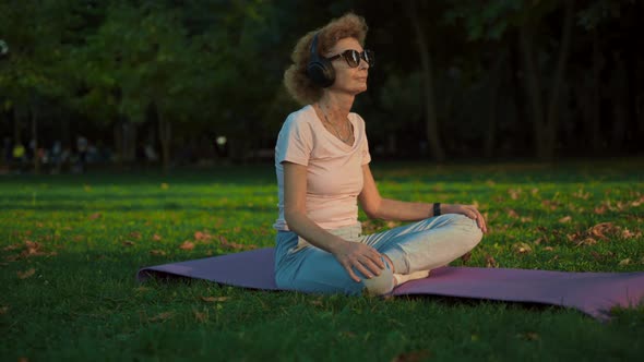 Joyful Peaceful Senior Woman Sitting in the Lotus Pose on Mat While Practicing Yoga Outdoors