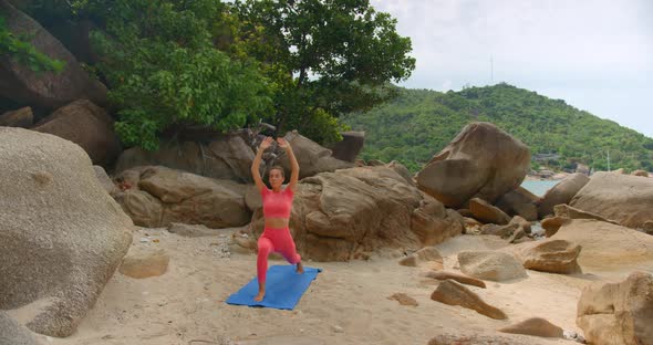 Woman Exercising on Blue Mat She Makes Warrior One Exercise on the Small Beach Between the Rocks