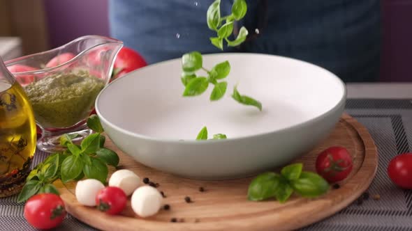 Making Caprese Salad  Fresh Basil Leaves Falling Into Ceramic Dish