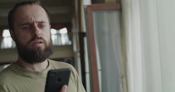 Handsome Man Has Emotional Conversation on a Mobile Phone in the Lobby at Window