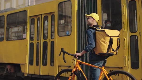 A Happy Delivery Man is Walking Through the Center of the Old Town and Holding a Bicycle with Him