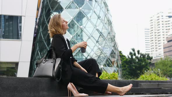 Happy Business Woman Taking Off Shoes And Resting With Coffee Outdoors