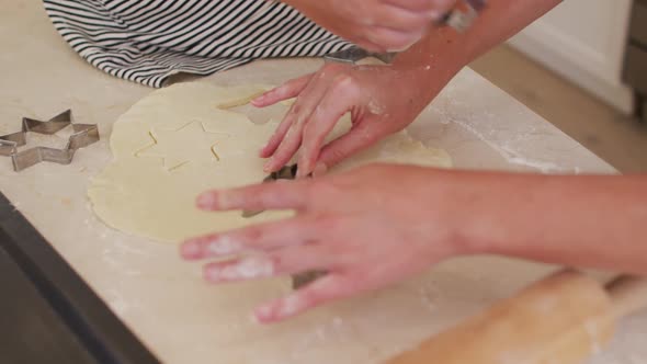 Mid section of mother and daughter cutting the dough with baking tin in star shapes in the kitchen