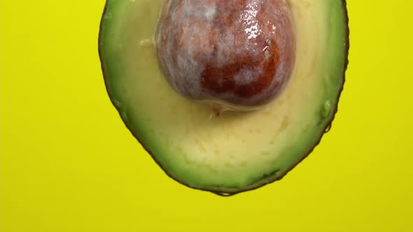 Water drops falling from avocado on yellow background. Avocado slice and water splashing, drops
