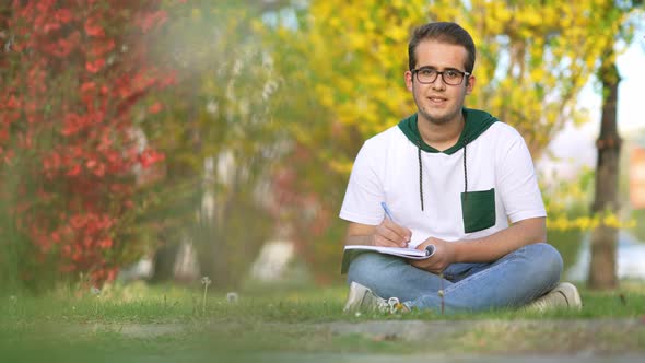University student sitting on grass, writing essay, literary studies project