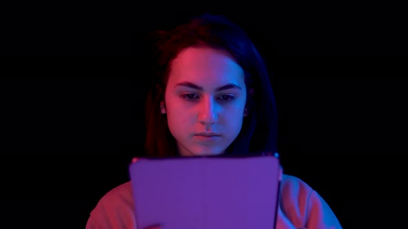 Young Woman with a Tablet. A Woman Is Using a Tablet. Blue and Red Light Falls on a Woman on a Black