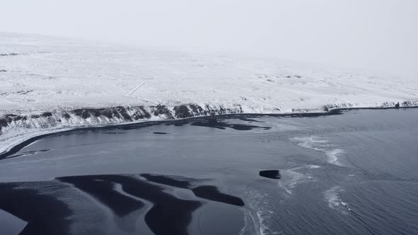 Drone Over Low Tide On Black Sand Beach And Snowy Landscape