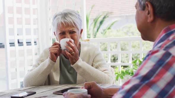 Happy senior mixed race couple having coffee talking in garden