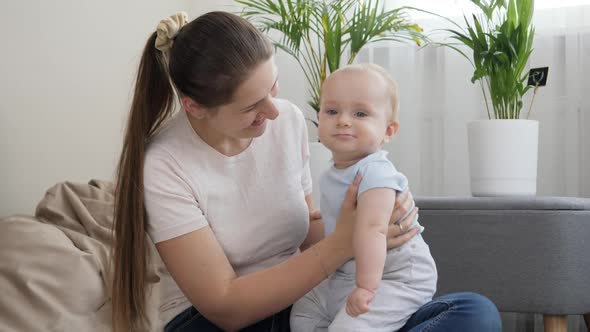 Happy Smiling Mother Holding and Rocking Her Little Baby Son on Lap in Living Room