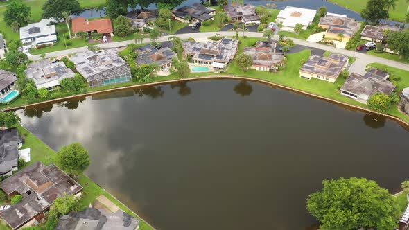An aerial view of a reflective pond, surrounded by nice houses and green grass on a sunny day. The c