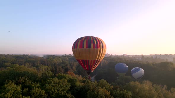 Colorful Hot Air Balloons Flying Over Green Park in Small European City at Summer Sunrise, Aerial