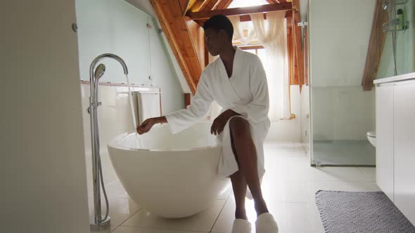 African american attractive woman in white robe sitting on bathtub, preparing bath