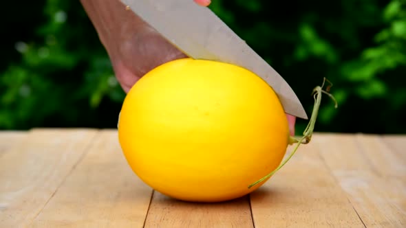 The man use knife split the orange melon on wood plate