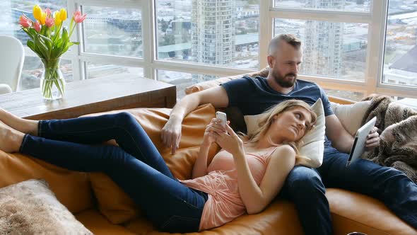 Couple using digital tablet and mobile phone in living room 4k