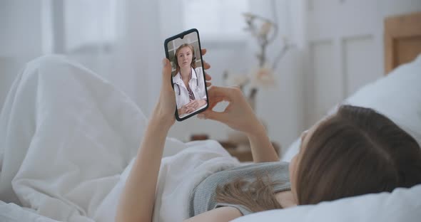 Female Lie in Bed at Home Using Smartphone To Talk To Her Doctor Via Video Conference Medical App