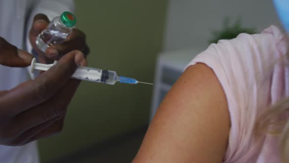 Caucasian female patient wearing face mask sitting in hospital bed getting injection