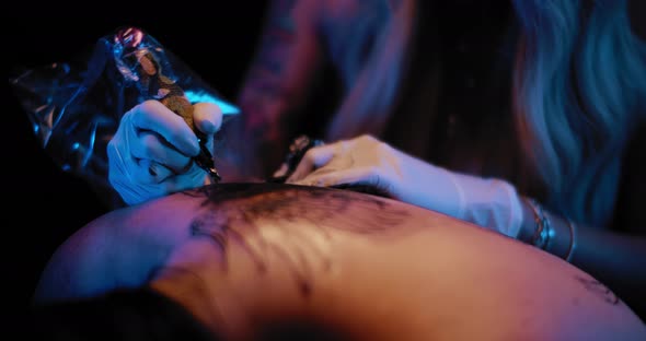 Close up of tattoo artist's hand making a big tattoo drawing on a person's back