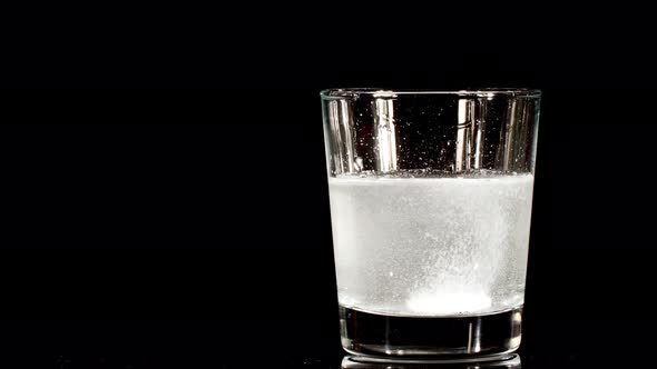 Pill Aspirin Falling Down in Glass with Water on Black Background