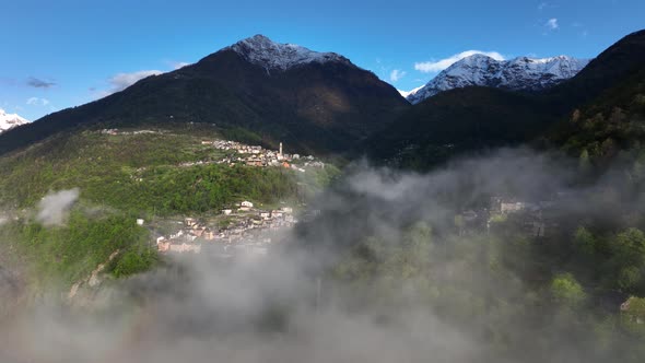 Flight through clouds with scenic view of Italian alp village in hillside; drone