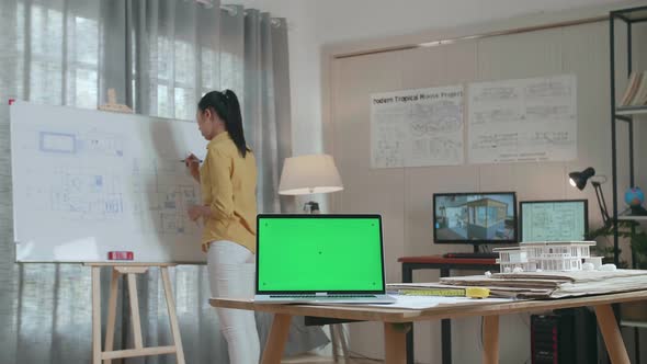 Asian Woman Engineer With Green Screen Laptop Drawing Blueprint On The Whiteboard At The Office