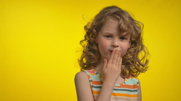 Little Curly Blond Girl in a Striped Dress is Blowing a Kiss and Smile