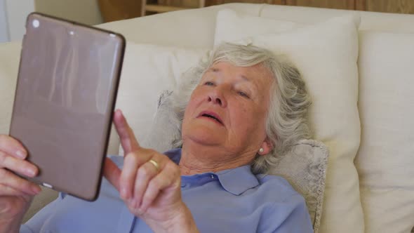 Caucasian senior woman smiling while using digital tablet lying on the couch at home