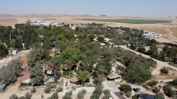 Aerial backwards panoramic drone shot of kibbutz Sde-Boker, filled with trees, bushes, fields, trail