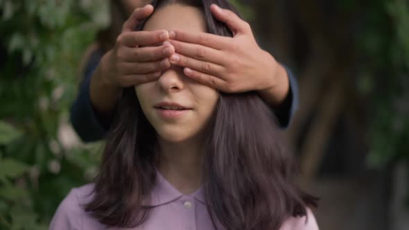 Closeup Portrait of Cheerful Teenage Girl in Park with Friend Covering Eyes with Hands