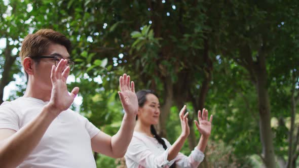 Happy asian couple exercising in garden with daughter, practicing tai chi together