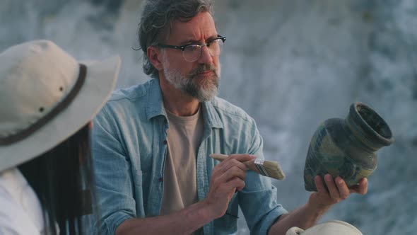 Mature Archaeologist Discussing Antique Vessel with Colleague