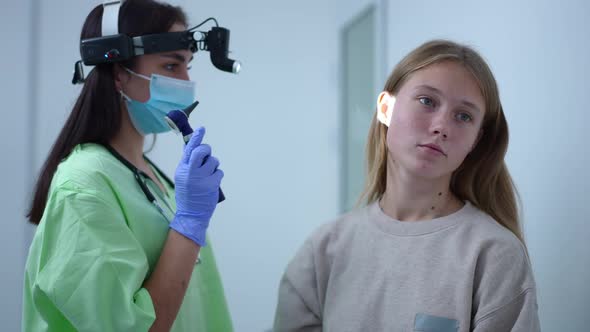 Teenage Caucasian Girl Sitting in Hospital As Otolaryngologist with Otoscope Entering Checking Ears