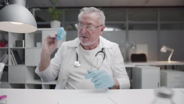 A Tired Elderly Experienced Doctor Nervously Removes His Latex Gloves After a Hard Days Work