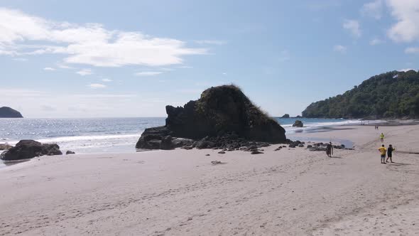 aerial drone shot on a white sandy beach rising over a rock towards the ocean