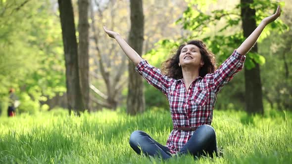 girl happily spreads her arms sitting in the park