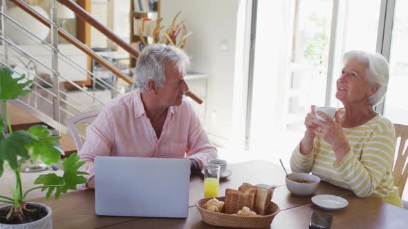 Senior caucasian couple talking to each other having breakfast together at home