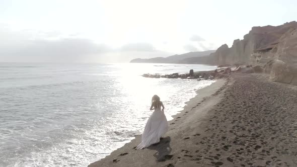 Aerial view of woman with wedding dress on beach Santorini island, Greece.