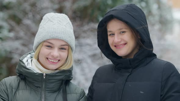 Closeup Portrait of Two Cheerful Young Women Posing in Snowfall in Fir Forest