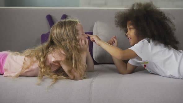 Cute multiracial best friends lying on sofa and having fun, childhood and joy