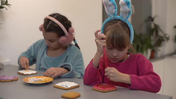 Two Little Sisters Decorating Homemade Cookies in the Kitchen at Home