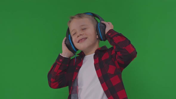 In Slowmotion on the Background of a Chromakey a Young Boy Listens to Music in Headphones and Dances