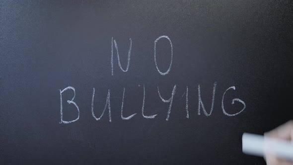 Hand writing no bullying on blackboard. Stop harassment. Human rights