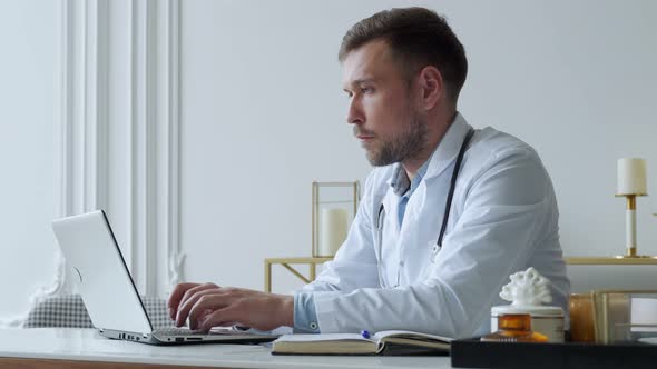 Concentrated Doctor Working with Laptop at Desk in Office