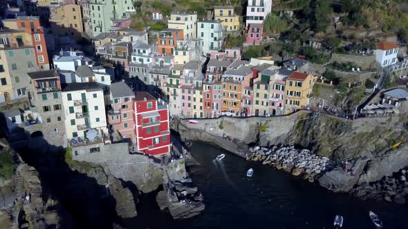 Town of Riomaggiore in the Cinque Terre Italian coast with boats and people, Aerial pan right shot