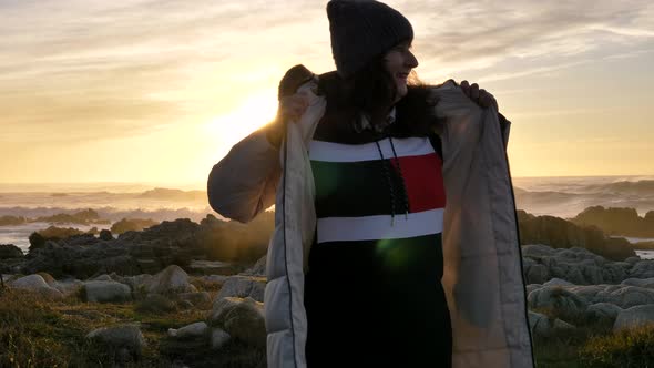 Mature Senior Caucasian Happy Woman Wearing Down Jacket Hat Beanie at the Sea with Slow Waves Ocean