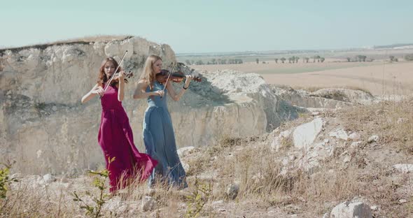Two Ladies in Blowing Dresses Play the Violin Among the Picturesque Rocks