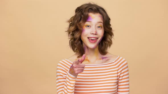 Portrait of Female Designer 20s with Multicolored Painted Spots on Face Smiling and Gesturing Finger