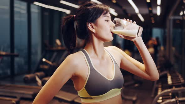 Attractive fitness asian woman finishing workout and drinking protein milk shake vitamins